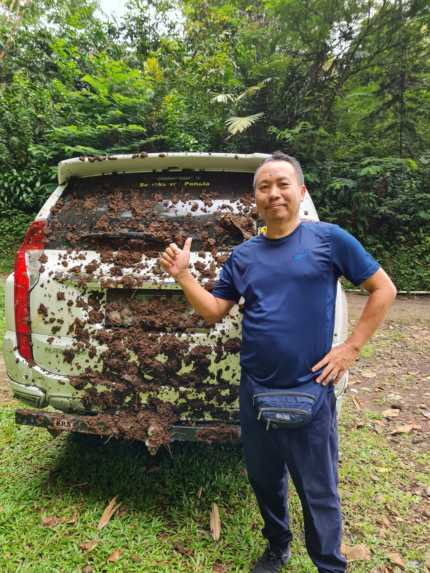 Papi berpose di samping mobil yang penuh lumpur setelah trekking