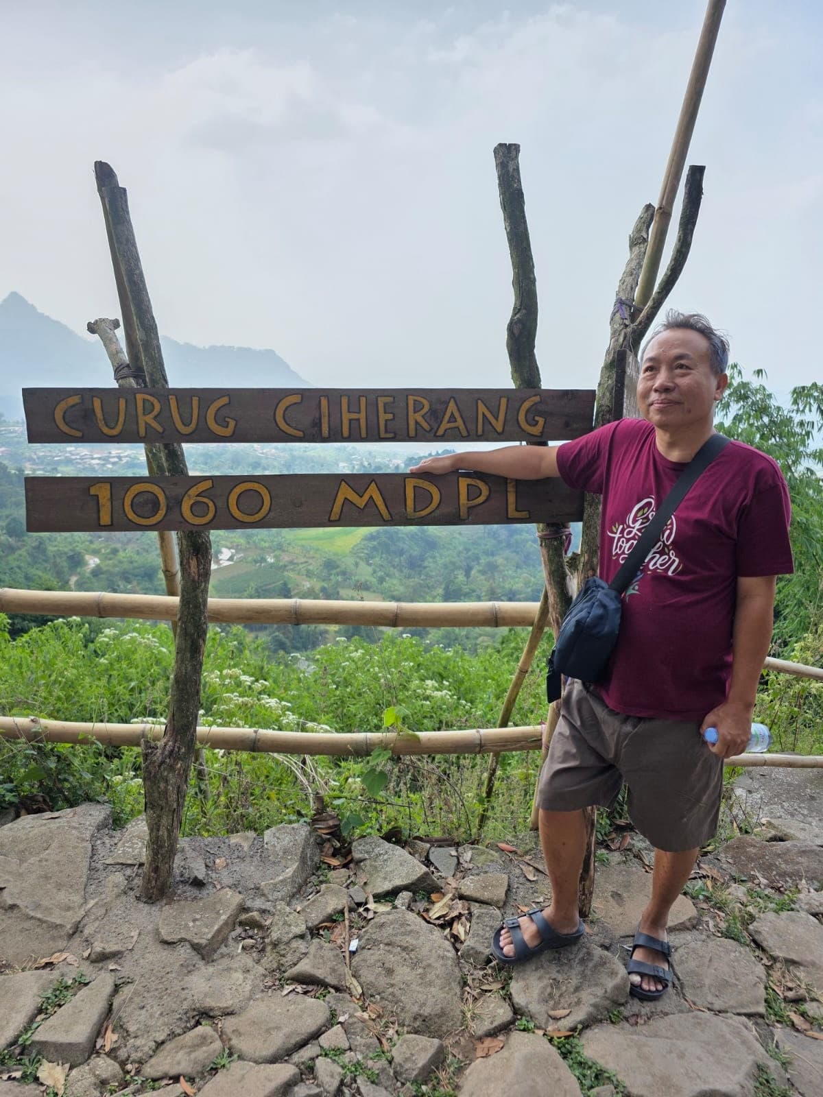 Papi berdiri di depan papan Curug Ciharang