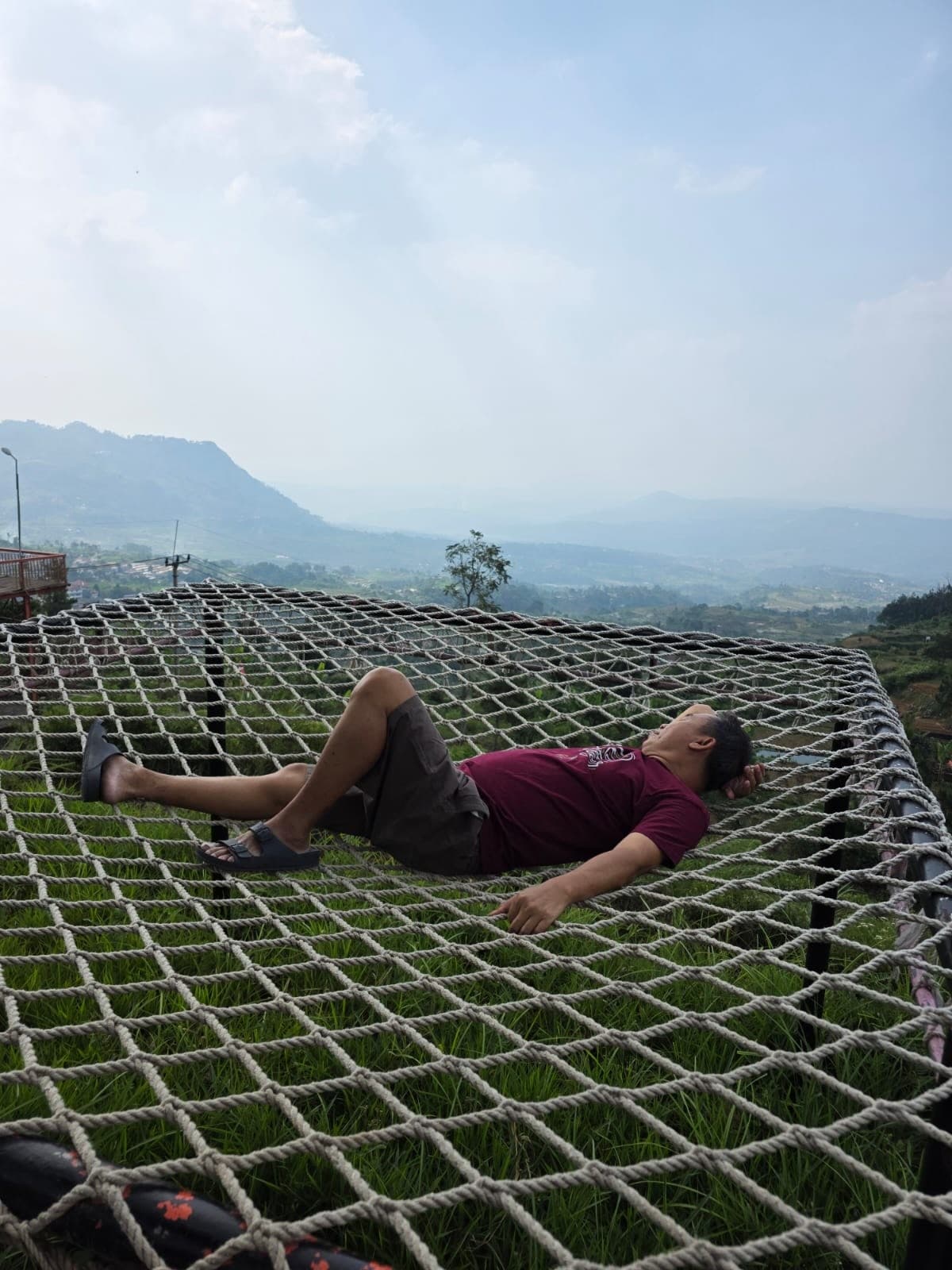 Papi bersantai di atas jaring dengan pemandangan pegunungan